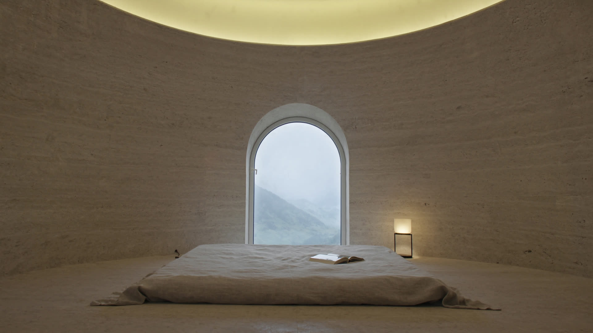 A curved travertine Engadin bedroom at first light, single arched window onto Alpine fog