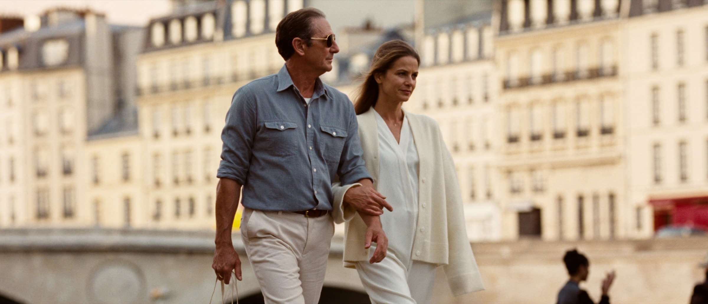 A couple in their late forties walking along a Parisian quay at golden hour, quiet luxury, no logos