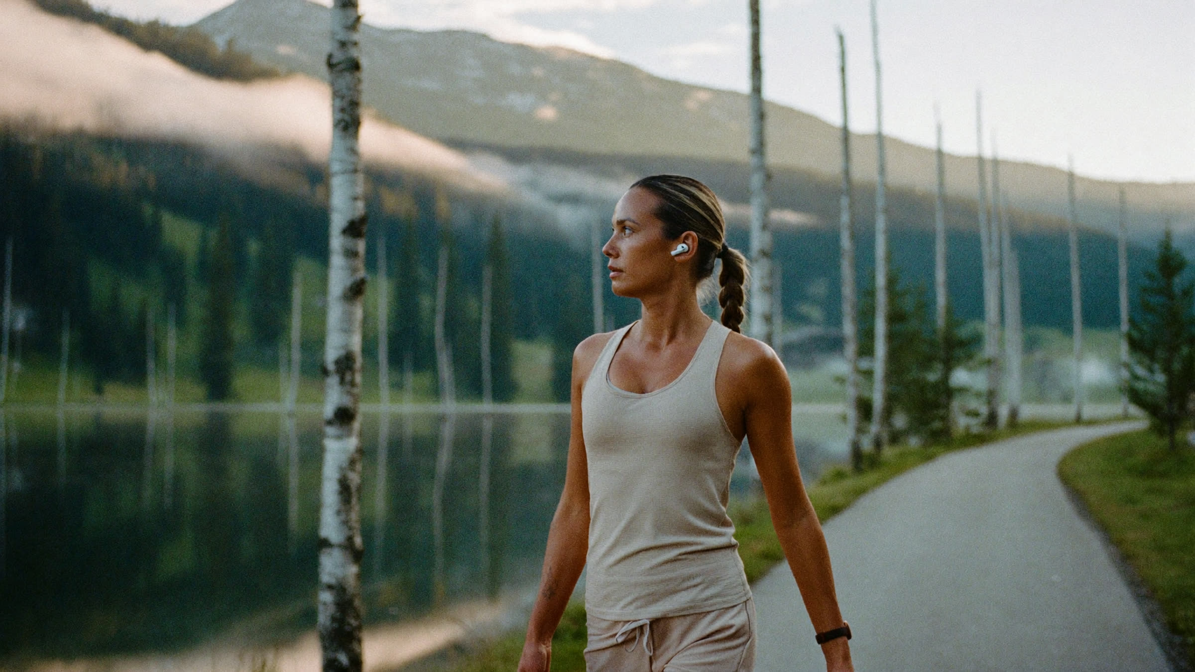 A woman in her late forties on a quiet Engadin lakeside path at first light, post-run, mountain mist behind