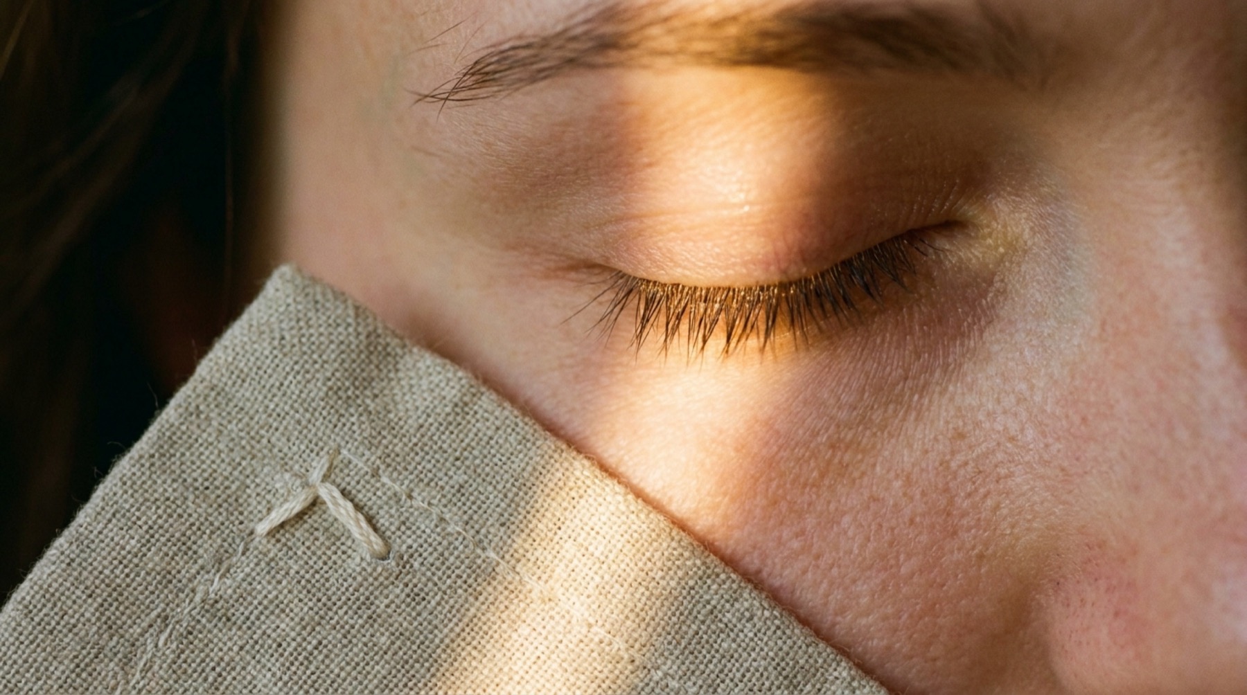 A closed eye in late afternoon light, edge of linen visible